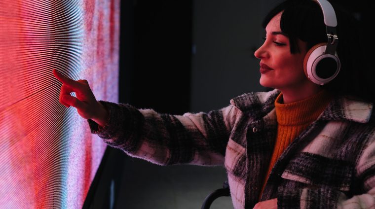 Woman in wheelchair reaching out to touch a colorful digital screen at an interactive art exhibit.